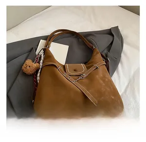 Detail of vintage brown tote with decorative straps, white stitching, and a plush bear charm