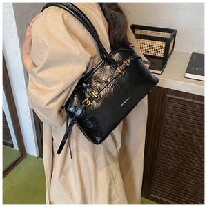 Detail of glossy black patent leather tote bag with gold eyelet buckle straps
