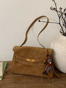 Vintage brown suede shoulder bag with gold clasp and plush bear charm on wooden surface