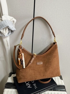 Braune Wildleder-Hobo-Tasche mit Perlenquaste und verstellbarem Gurt auf Koffer
