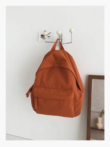 Close-up of minimalist orange canvas backpack hanging on a hook in a home setting