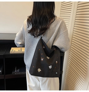 Detail of black canvas tote bag with colorful cat embroidery and brown leather straps