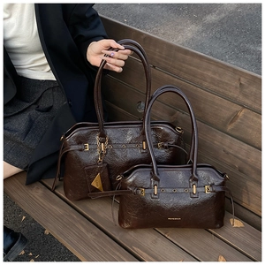 Detail of dark brown glossy leather tote bags with gold hardware on a wooden bench