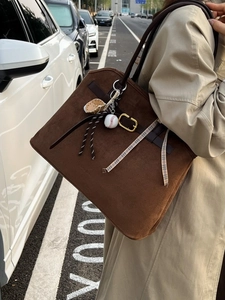 Brown suede tote bag with baseball charm and ribbon in a street style fashion setting
