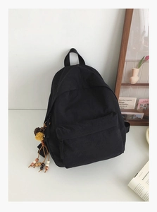 Detail of minimalist black backpack with decorative tassel and front zipper pocket