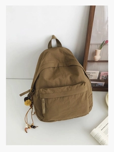 Detail view of khaki nylon backpack with decorative colorful wooden beads and pom-poms