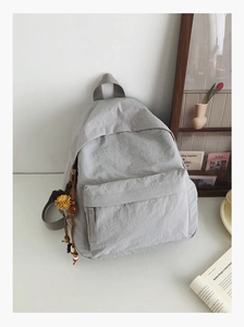 Detail of light gray nylon backpack with decorative flower charm and natural texture
