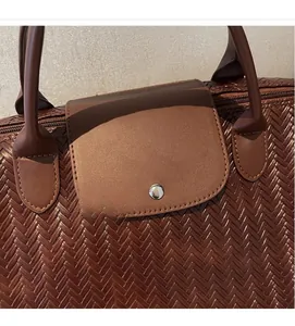 Détail du sac de voyage marron tressé avec rabat en cuir et fermeture métallique