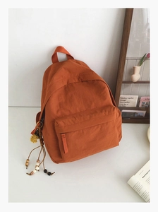 Close-up of orange backpack with colorful bead tassels and stylish front zipper pocket