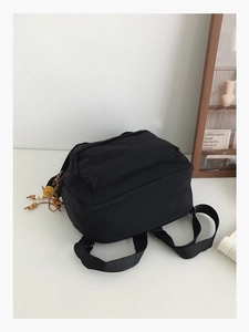 Detail of minimalist black nylon backpack with decorative wooden bead and yellow pompom charm