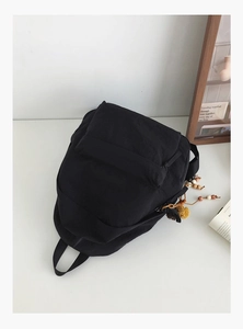 Close-up of minimalist black backpack with cute beaded flower charm in a cozy indoor setting