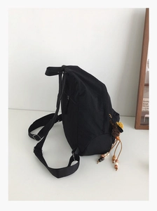 Detail of black nylon backpack featuring a side anti-theft pocket and ethnic style charm