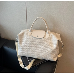 Détail du sac de voyage tressé blanc cassé avec rabat en cuir et bandoulière amovible
