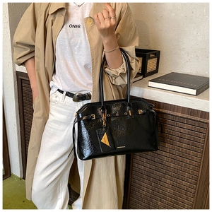 Close-up of black patent leather tote bag with glossy texture and gold metal buckle detail