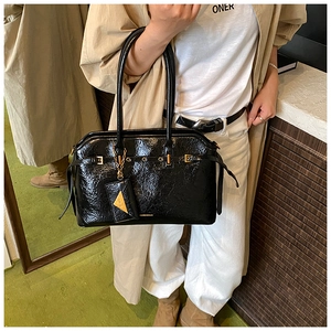 Close-up of black glossy wrinkled patent leather tote bag with gold metal buckle hardware
