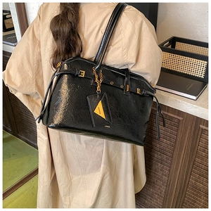 Detail of black glossy tote bag featuring fine pleated texture and golden metal hardware