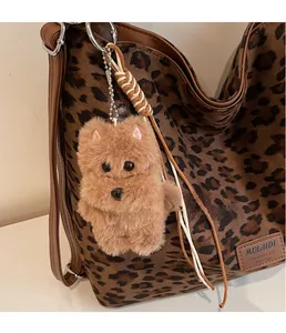 Detail of a brown plush dog charm with metal chain and braided rope on a shoulder bag