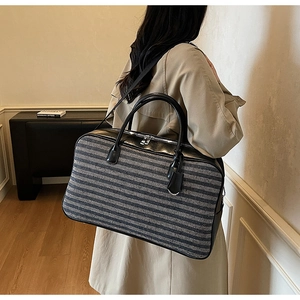 Détail d'un grand sac de voyage bicolore rayé avec poignées en cuir et bandoulière amovible