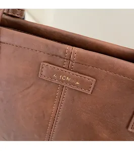 Close-up of golden ZHCNMA logo on premium brown lychee texture leather handbag
