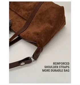 Detail view of reinforced shoulder straps and metallic hardware on brown suede handbag