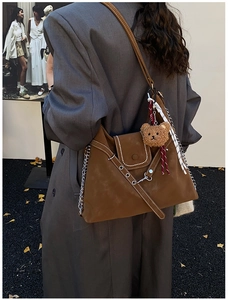 Detail of brown suede crossbody bag featuring metal chain accents and a plush bear charm