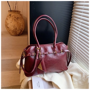 Detail of burgundy wax leather tote bag with elegant buckle and logo tag in soft light