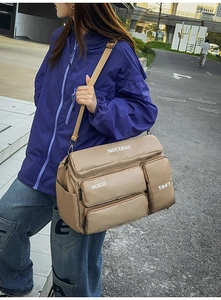 Close-up of khaki multi-pocket nylon travel bag with wide strap and metallic buckles