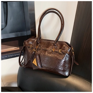 Detail of dark brown glossy patent leather tote with gold hardware and fashion charm