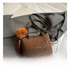 Détail d'un sac seau léopard marron foncé avec pompon et accessoire à pompons en cuir