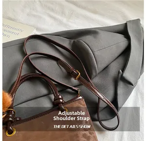 Détail d'une bandoulière réglable avec boucle en métal doré sur un sac seau marron en daim