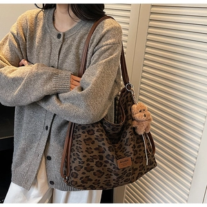 Detail view of leopard print tote bag with brown leather strap and teddy bear charm