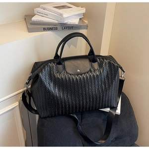 Détail d'un sac de voyage noir tissé avec rabat en cuir et fermeture par bouton-pression