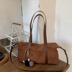 Detalle de bolso de hombro en ante marrón oscuro con correa larga y pompón decorativo