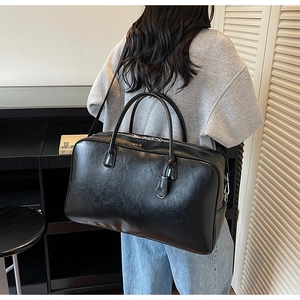 Vue arrière détaillée d'un grand sac cabas en cuir noir porté à l'épaule par une femme