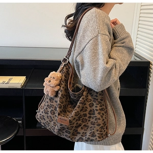 Detailed view of leopard print shoulder bag with plush bear charm and leather brand logo
