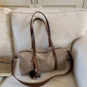 Primer plano del bolso Boston de ante caqui con asas de cuero y detalles de flecos