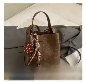 Detail of dark brown faux crocodile bucket bag with leopard heart charm and long strap