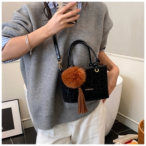 Détail du sac à main noir gaufré léopard avec grosse boule de fourrure brune et pompon