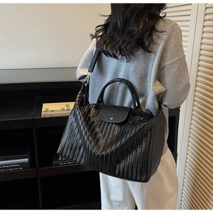 Détail du grand sac cabas noir tressé avec rabat en cuir porté par un mannequin