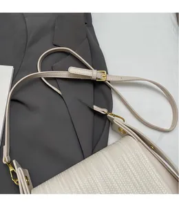 Detail of cream woven crossbody bag featuring adjustable strap and gold hardware accents