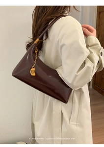 Detail of dark brown leather baguette bag featuring gold chain and crescent moon pendant