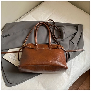 Detail of a brown oil wax leather tote bag with gold hardware on a grey blazer background