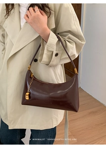 Detail of dark brown leather baguette bag with a gold pea pendant and metal chain accent