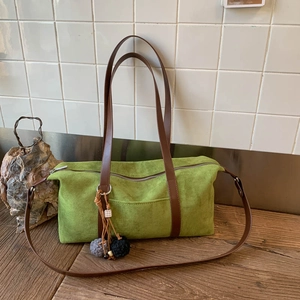 Detalle de bolso bandolera vintage verde mate con asas de cuero marrón y adorno de pompón