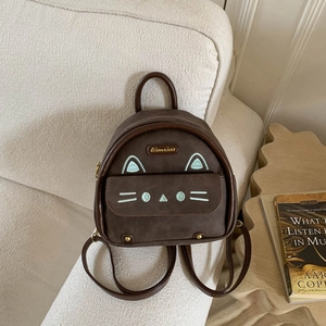 Detail of a dark brown suede cat backpack featuring embroidered ears and a metal logo