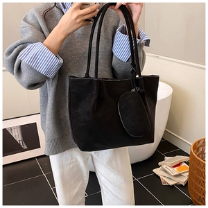 Detail of a black matte leather tote bag with a matching round coin purse on a model