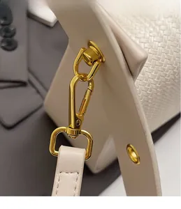 Detail of gold metal hook hardware on beige woven texture crossbody bag with fine stitching