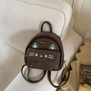 Close-up of a brown suede cat-themed mini backpack on a cream sofa with subtle embroidery