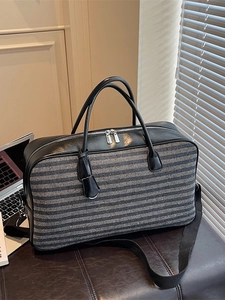 Sac de voyage rétro bicolore en toile et cuir posé sur un banc en cuir dans un bureau