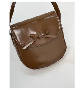 Detail of dark brown glossy saddle bag featuring a stylish leather bow and retro texture